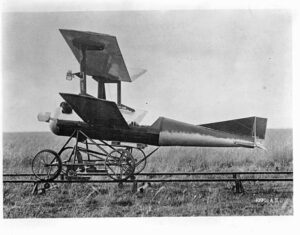 Black and white historical photo of an experimental airplane with wings mounted above its body, standing on a rail-mounted carriage in an open field.